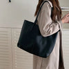 A woman is holding a large black leather tote bag with a shoulder strap, next to white cabinetry.