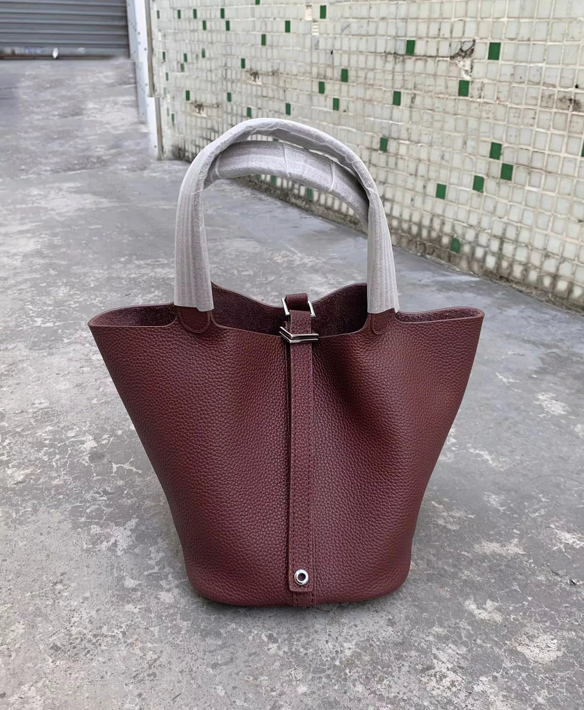 Tiefburgunder roter Leder-Bucketbag mit hellem grauem Stoffgriff auf Beton