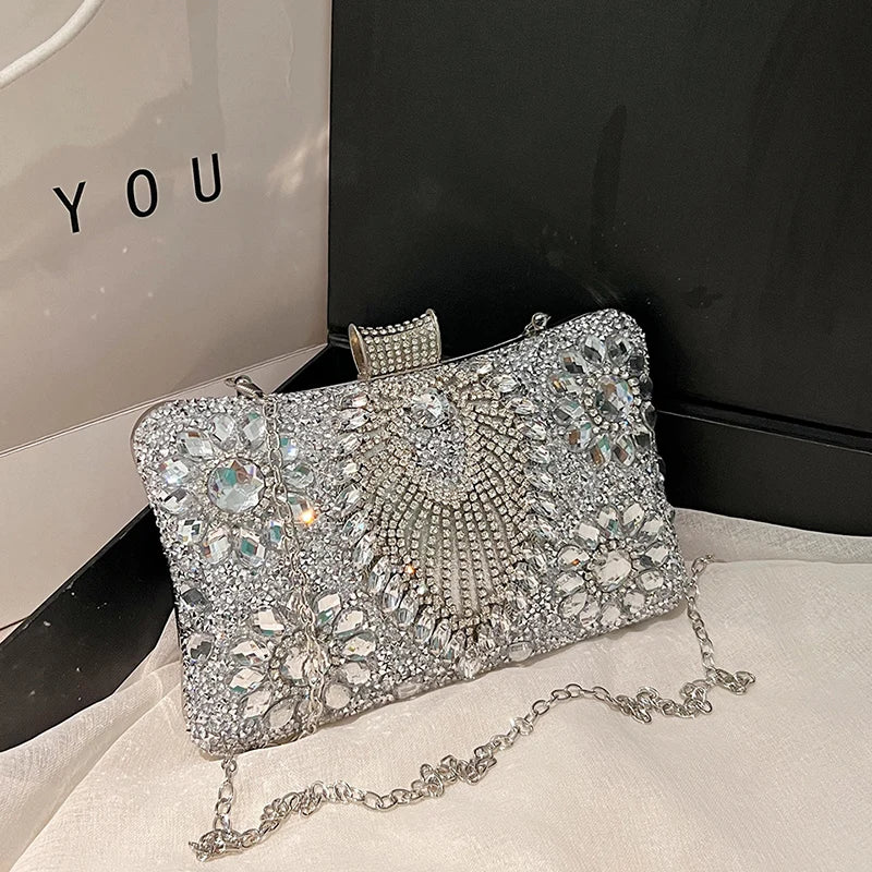 A silver rhinestone evening clutch bag with a textured surface and a chain is displayed on a white fabric.