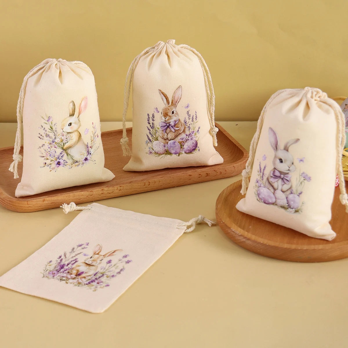 A set of six light beige drawstring gift bags featuring illustrations of rabbits and purple flowers.