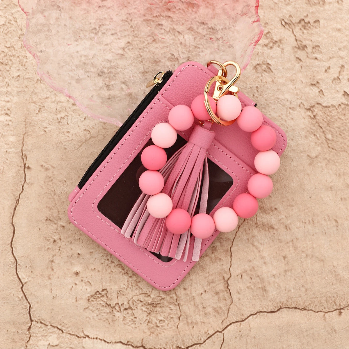 A pink leather card holder with a tassel bangle keychain rests on a textured background.