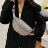 A woman holds a silver rhinestone-embellished crossbody waist bag with an adjustable strap against a black blazer.