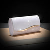 A white envelope clutch with a gold chain detail resting on a wooden surface.
