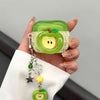 A hand holds a green apple shaped earphone case with a yellow accent, featuring a small charm.
