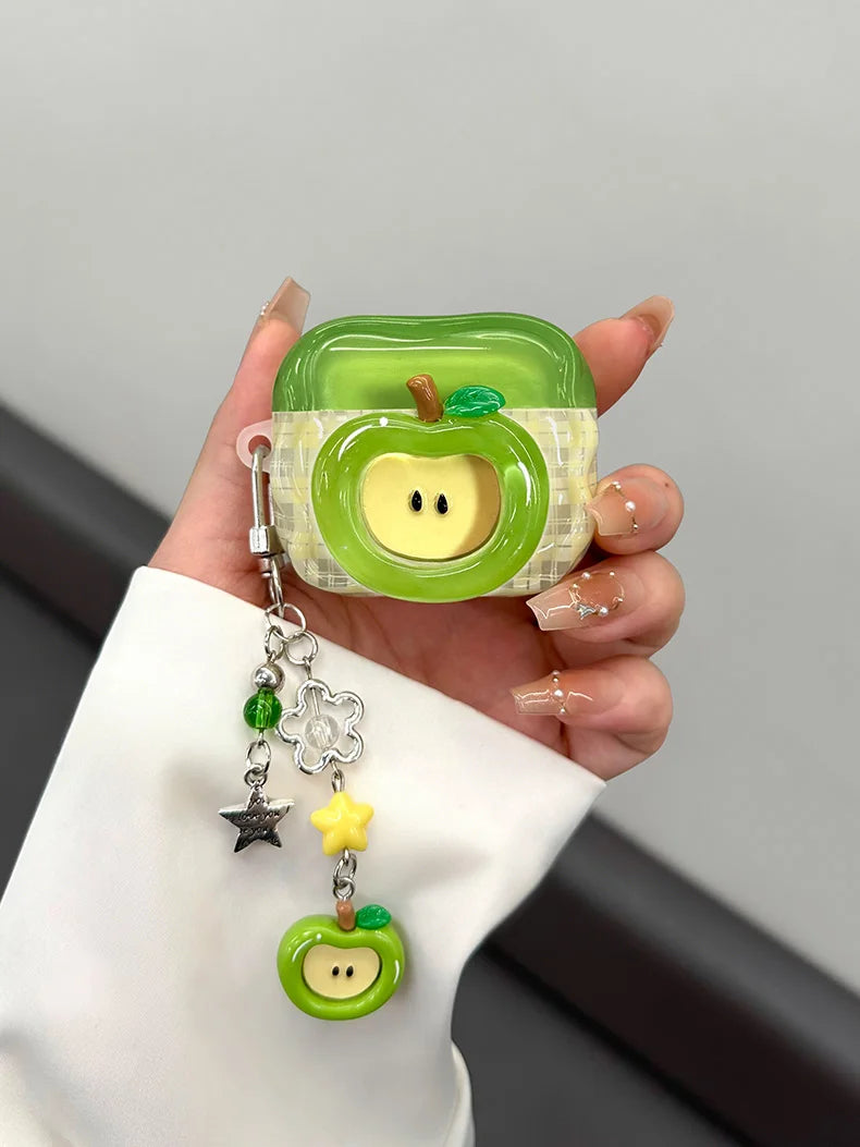 A hand holds a green apple shaped earphone case with a yellow accent, featuring a small charm.