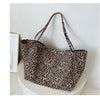 A leopard print canvas crossbody tote bag with brown and black spots, displayed on a white surface.