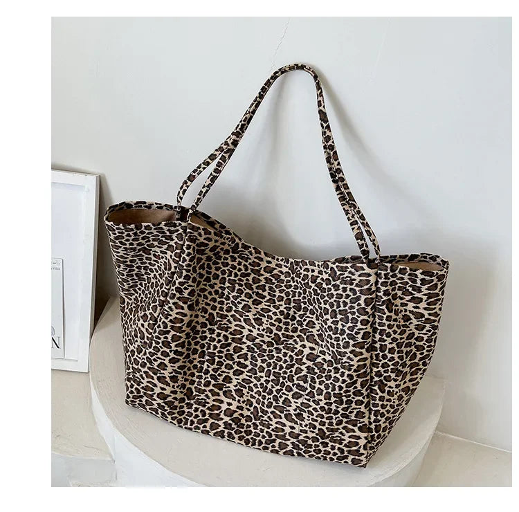 A leopard print canvas crossbody tote bag with brown and black spots, displayed on a white surface.
