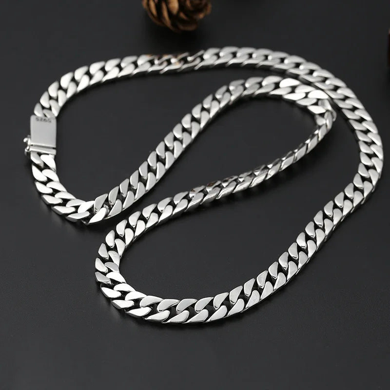 A silver punk charm bracelet with a padlock clasp is laid out on a dark surface.