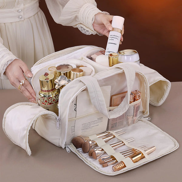 A hand is placing a tube of cream into a portable side-zip cosmetic organizer bag filled with makeup brushes and tools.