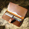 A brown genuine leather long bi-fold wallet with a snap closure, displaying cards and cash on a textured paper background.
