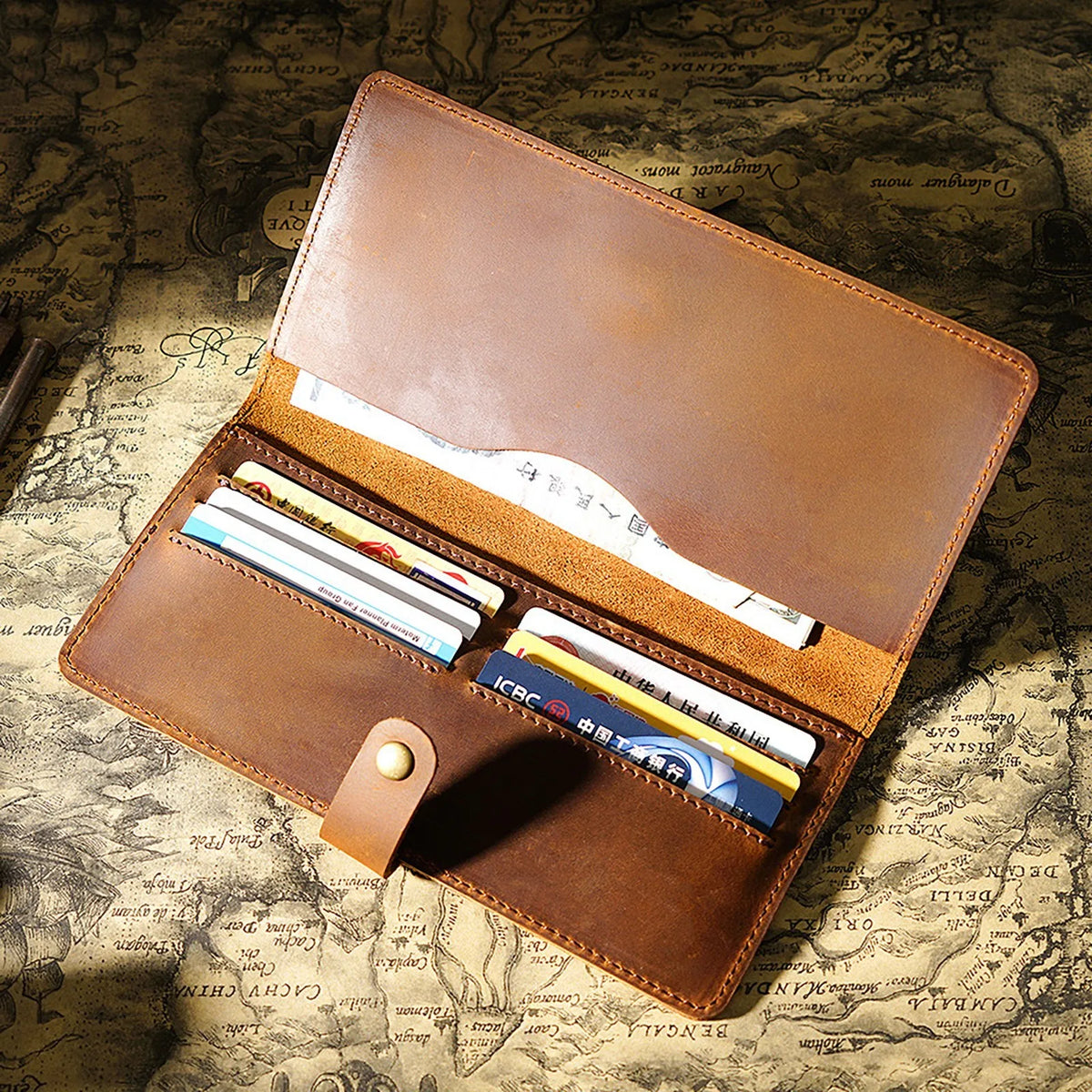 A brown genuine leather long bi-fold wallet with a snap closure, displaying cards and cash on a textured paper background.