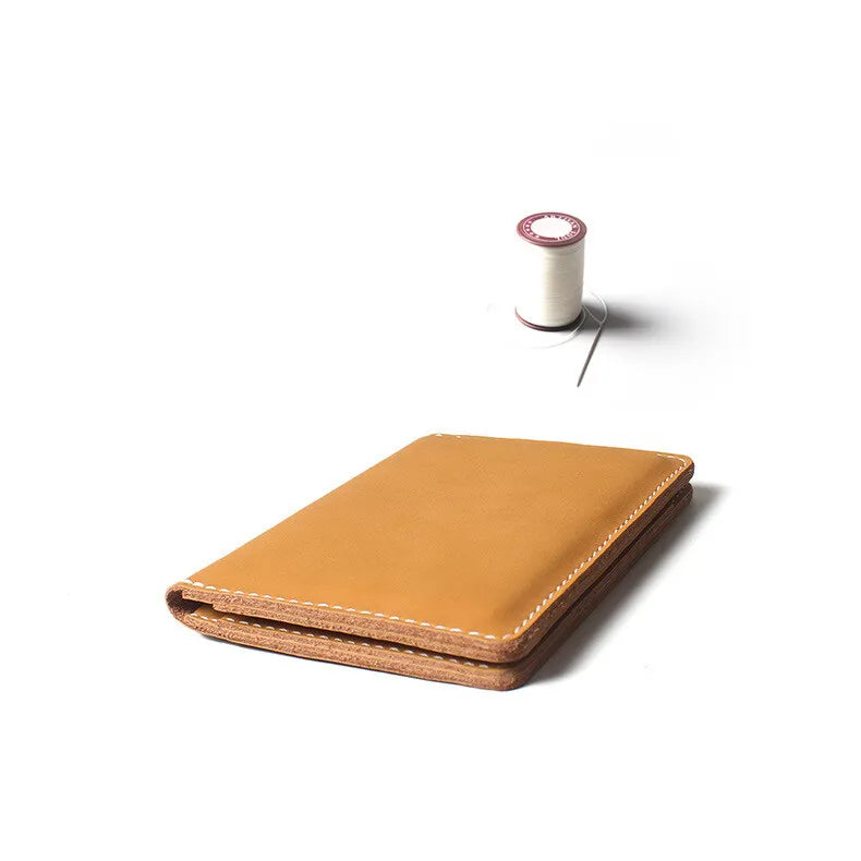 A tan genuine cowhide leather passport and ticket holder with a stitched edge, next to a roll of white tape.