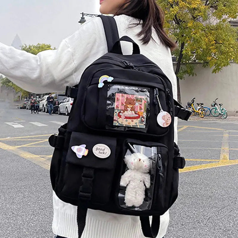 A woman is wearing a black Korean style large capacity backpack with various compartments and cute charms.
