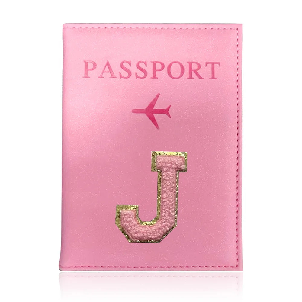 A pink leather passport holder with a gold initial J and a pink airplane emblem.