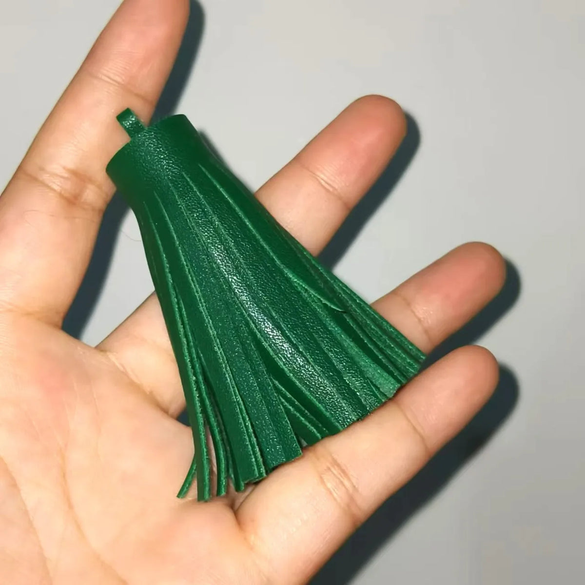 A hand holds a vibrant green leather tassel fringe craft supplies set.