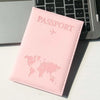 A pink passport holder with a world map design resting on a white surface next to a laptop keyboard.