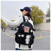 A woman wearing a white sweater and blue hat carries a large black backpack outdoors.