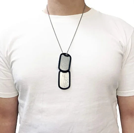 A close-up of a personalized military dog tag necklace set with two oval pendants on a white t-shirt.