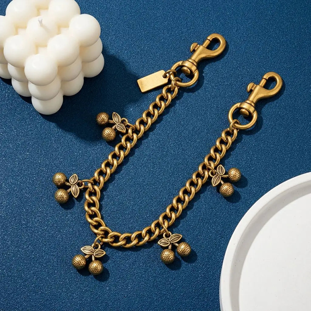 Colgante de bolso de cadena de cereza vintage dorada sobre una superficie azul oscuro junto a cuentas blancas.