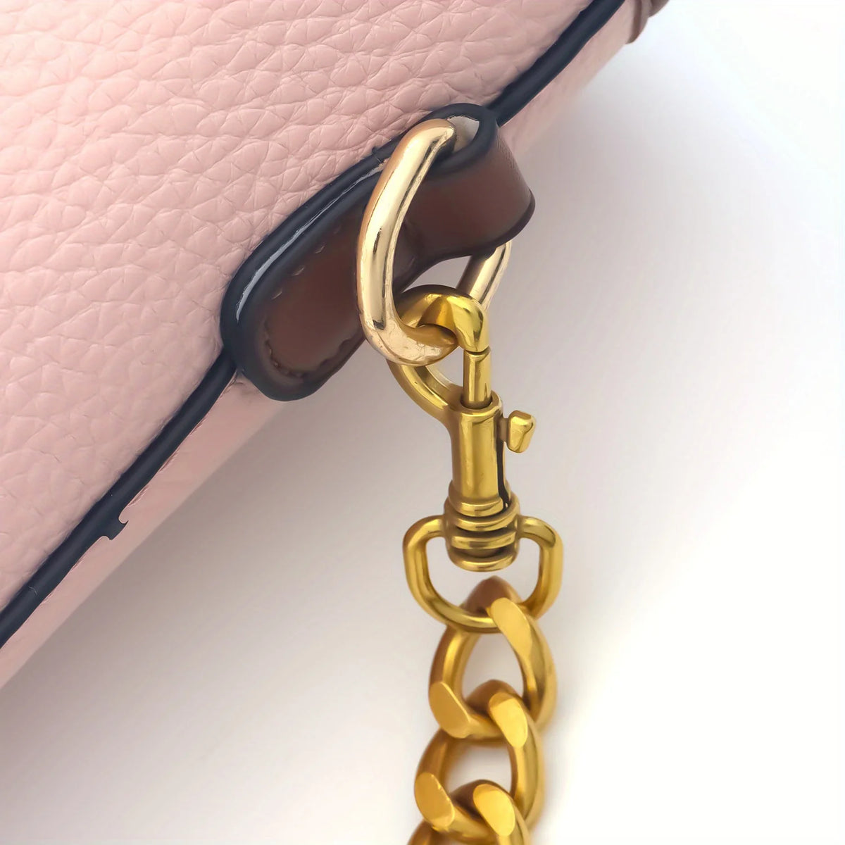 A close-up of a thick gold metal chain replacement strap attached to the corner of a pink leather purse.