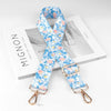 A light blue floral patterned diagonal shoulder strap for bags displayed on a white box.