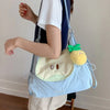 A person is holding a light blue nylon messenger backpack with a yellow fruit charm.
