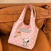 A pink canvas shoulder bag featuring a Snoopy cartoon character resting on a brown couch.