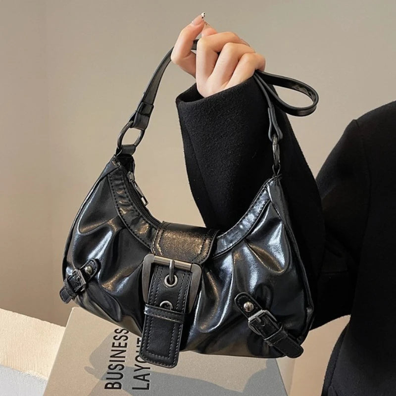 Nahaufnahme einer schwarzen Leder-Y2K-Retro-Plium-Schultertasche, gehalten von einer Person in einem schwarzen Blazer.
