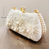 A white clutch bag with delicate floral embroidery and a pearl chain strap, shown in profile.