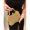 A hand holds an elegant gold diamond rhinestone evening clutch bag with a golden tassel.