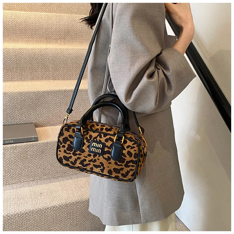 Eine Frau hält eine braune Leopardenmuster-Designer-Hobo-Tasche vor einem hellgrauen Mantel auf der Treppe.