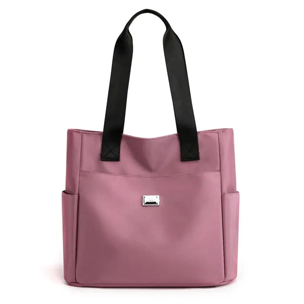 A pink nylon shoulder tote bag with black straps.