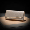 A rectangular envelope clutch with a textured gold glitter finish and a gold-toned chain resting on a wooden surface.