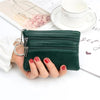 A dark green PU leather clutch wallet is held by a hand next to a white cup and some papers.