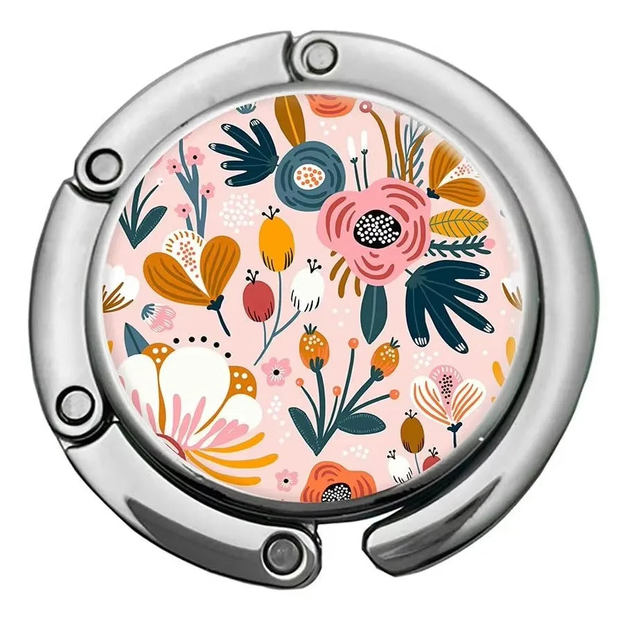 A close-up of a silver bag hook with a circular, multi-patterned floral design on the surface.