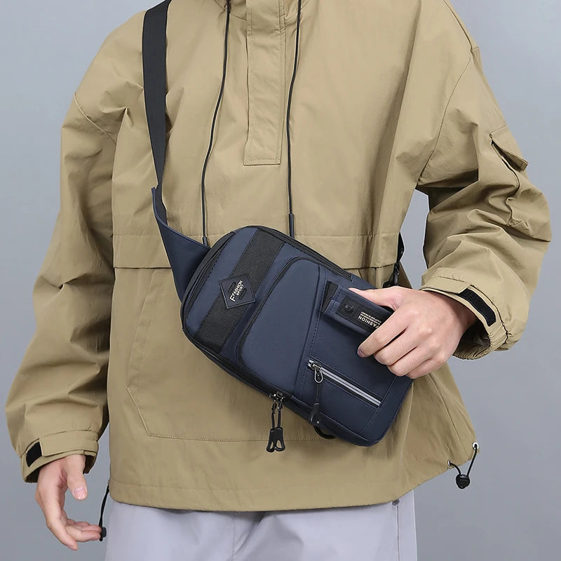 A man wearing a tan jacket holds a navy blue nylon crossbody sling bag.