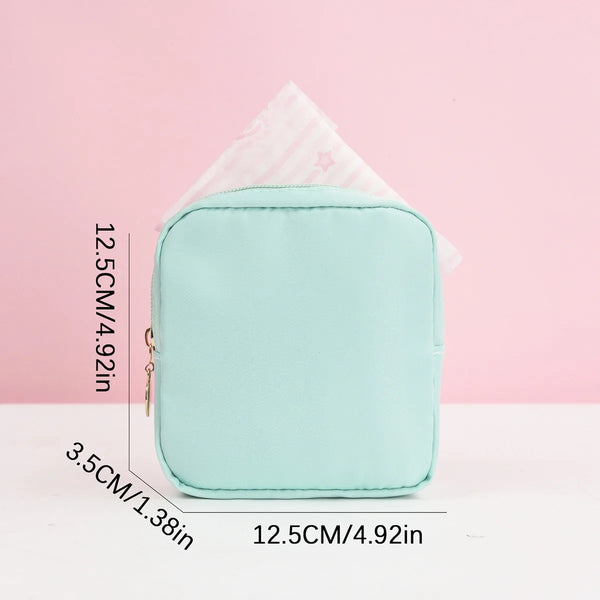 A light mint green portable pouch for storing sanitary napkins, shown next to a triangular tissue.