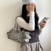 A person wearing a polka dot headband holds a leopard print Rivet Boston shoulder bag to their face.