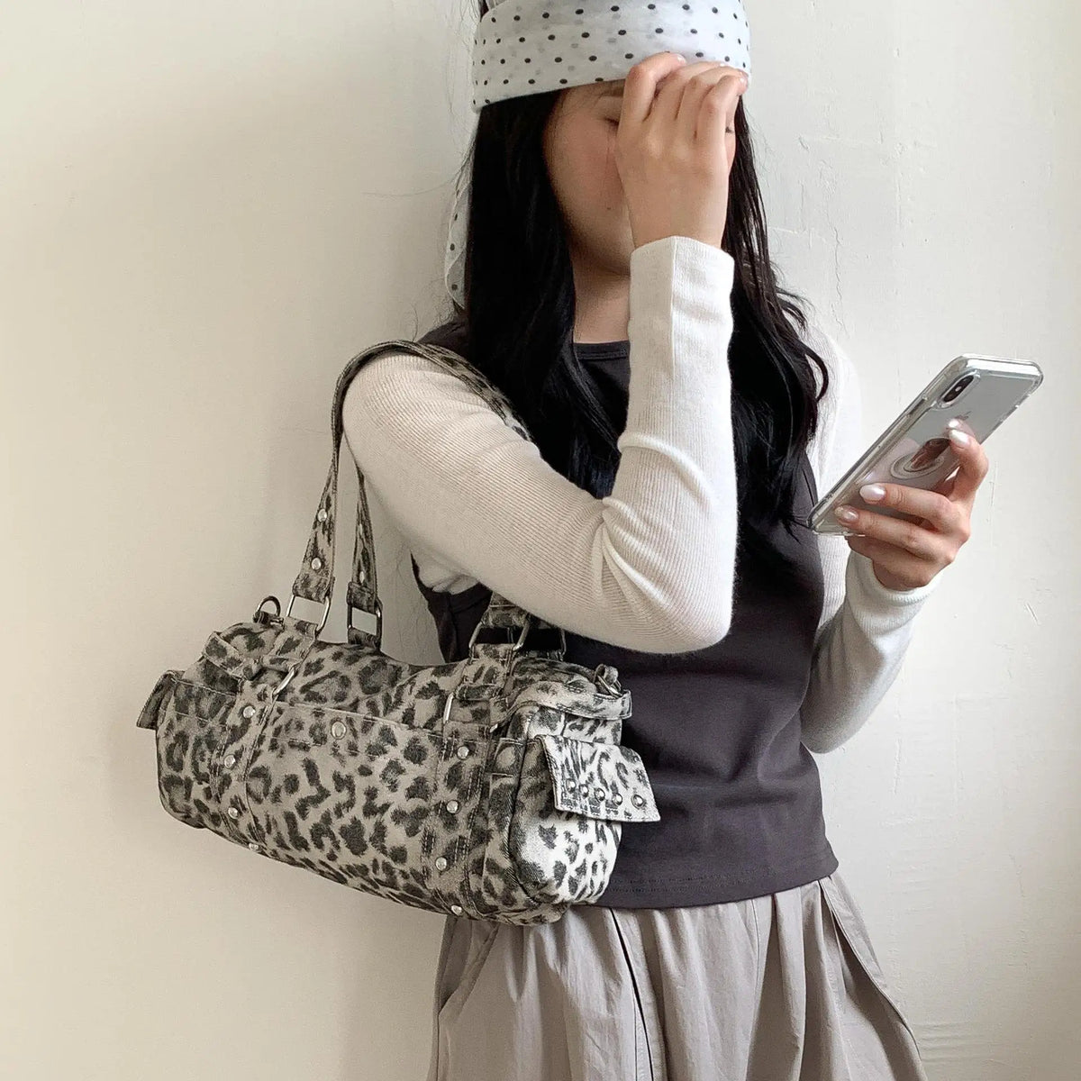 A person wearing a polka dot headband holds a leopard print Rivet Boston shoulder bag to their face.