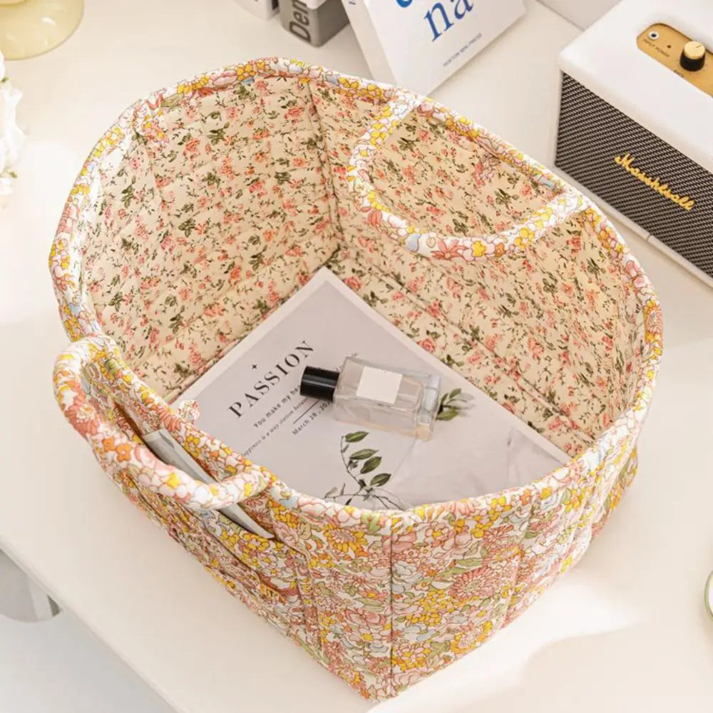 A quilted fabric storage basket with carry handles, featuring a floral pattern, is shown on a white surface.