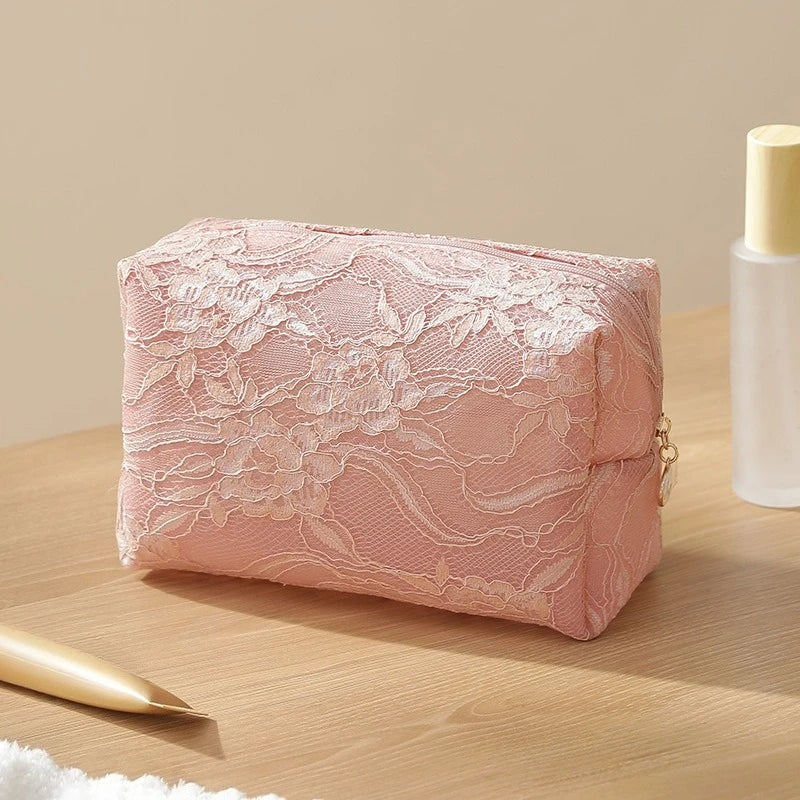 A pink lace mesh cosmetic and jewelry organizer bag resting on a wooden surface next to a glass bottle.