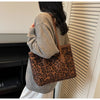 A person wearing a grey sweater holds a brown leopard print vintage tote bag against a white slatted background.