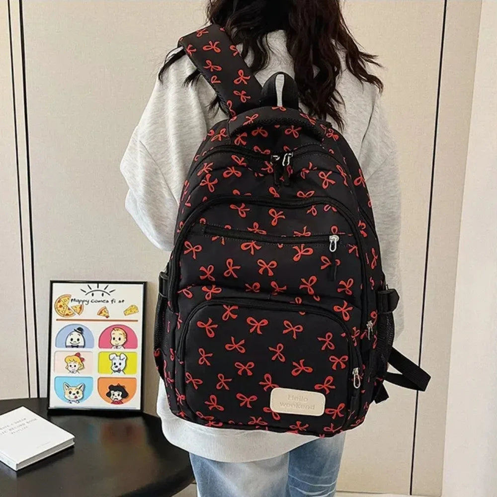 A black nylon travel backpack with a red bow print is worn by a person.