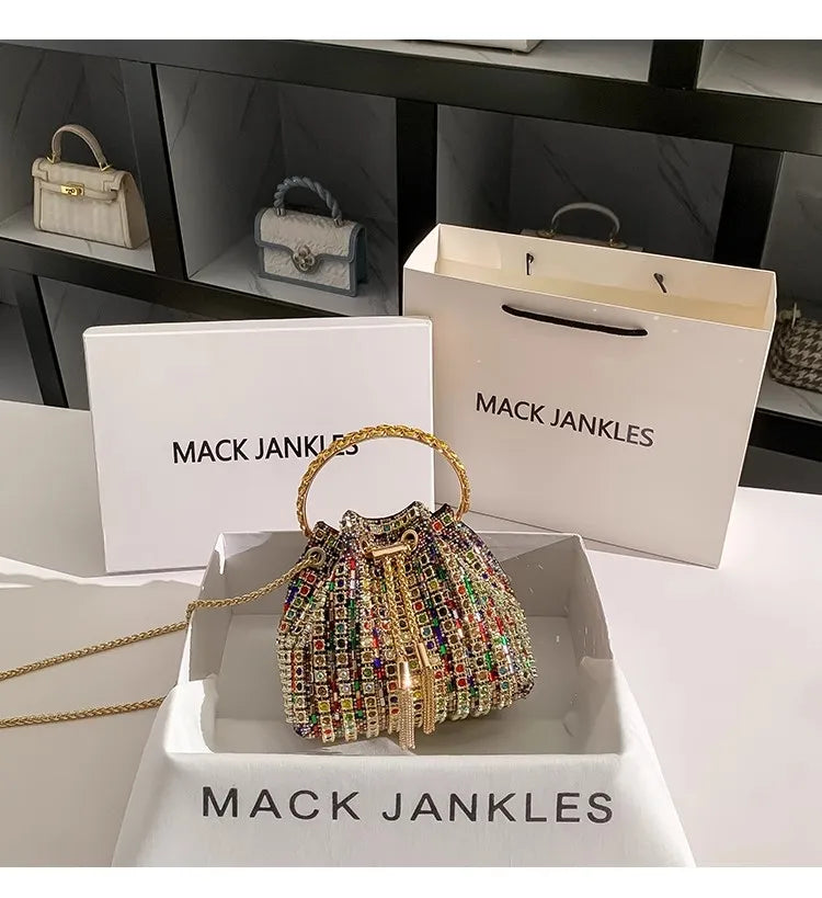 A gold chain crystal-embellished evening clutch displayed in a white box with the Mack Jenkins brand visible.