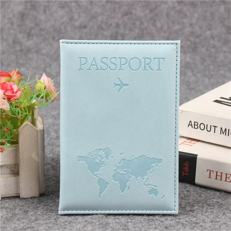 Couverture de passeport en cuir PU bleu clair avec texte gravé et un petit avion sur une surface grise.