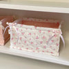 A white quilted cotton storage basket with a pink lace flower design is displayed on a shelf.