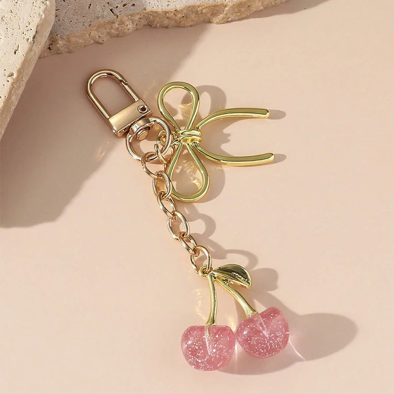 Pendentif de cerise rouge doré avec boucle de homard et chaîne, posé sur un fond clair.