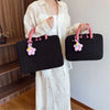 A woman holds a black quilted laptop sleeve with pink charm and a white dress.