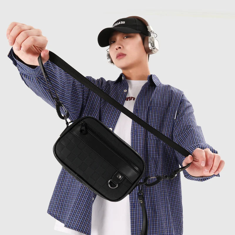 A person holds up a black PU leather crossbody bag with an adjustable strap against a light background.