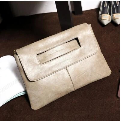 A beige leather crossbody clutch bag resting on a dark brown surface with shoes in the background.